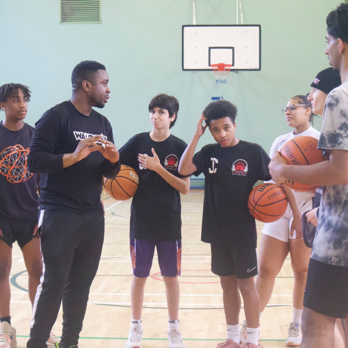 Coach talking to young academy players holding basketballs